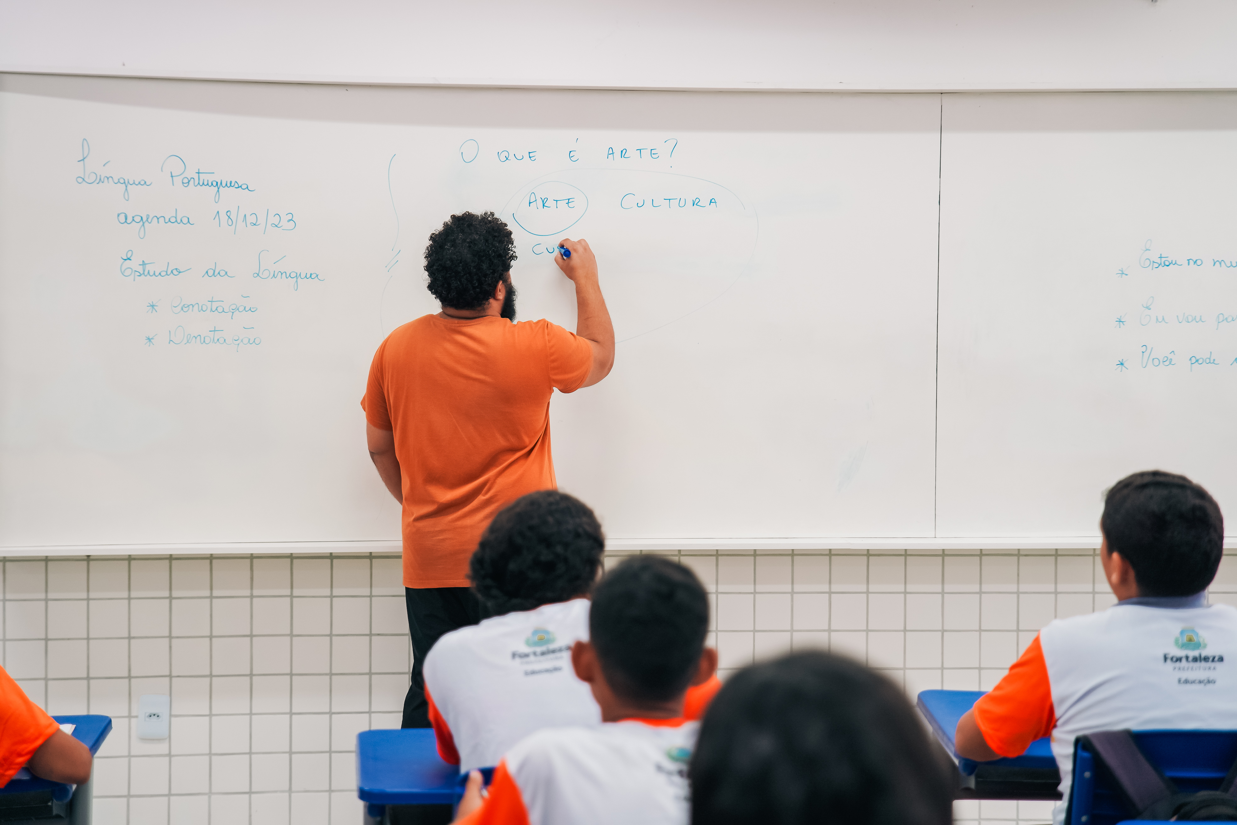 professor de costas escreve numa lousa branca na sala de aula